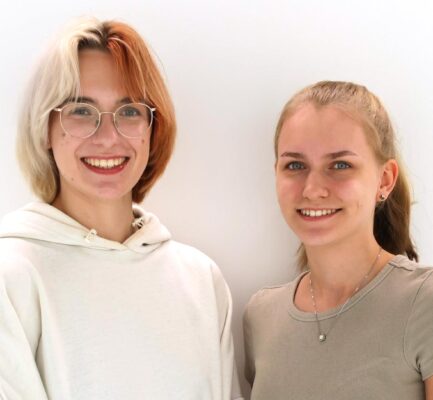 Zwei junge Frauen vor weißem Hintergrund lächeln in die Kamera