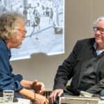 Nidecken und Wirdeier im angeregten gespräch, hinten Schwarzweißfoto an der Wand