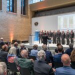 Blick über das pUblikum auf die Bühne, wo rund 18 Sänger in Anzug und roter Krawatte performen